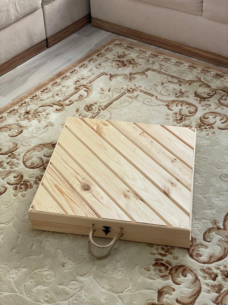 May include: A wooden storage box with a hinged lid and rope handles. The lid has a diagonal pattern of wood planks.