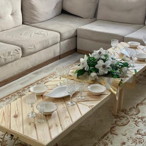 May include: A wooden table with a chevron pattern top, set for a meal with white plates, bowls, and glasses. A bouquet of white flowers sits in the center of the table.