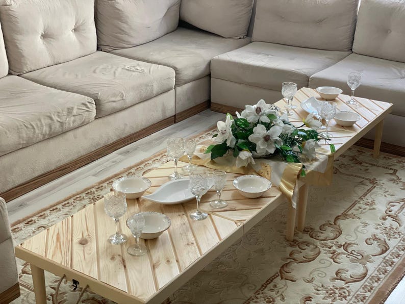 May include: A wooden table with a chevron pattern top, set for a meal with white plates, bowls, and glasses. A bouquet of white flowers sits in the center of the table.