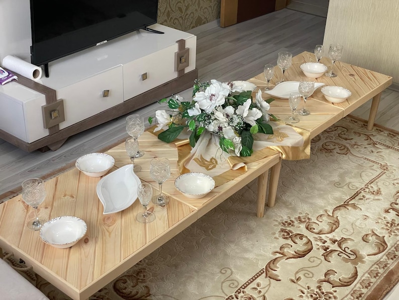 May include: A wooden table set with white plates, bowls, and glasses. A bouquet of white flowers sits in the center of the table, surrounded by gold fabric.