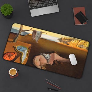 May include: A rectangular mouse pad featuring a surrealist painting with melting clocks, a barren tree, and a landscape with a warm color palette. The design includes a white computer mouse and a black border.