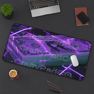 May include: A rectangular mouse mat with a purple and teal design featuring a stack of dollar bills and lightning bolts. The text "CraftyPadCo" is repeated across the mat. A white mouse is on the right.