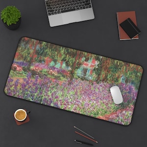 May include: Rectangular mouse pad featuring a colorful impressionist painting of a garden with purple flowers, green foliage, and a red bridge. A white mouse is on the right side of the pad. The pad is on a dark surface with a laptop, coffee cup, and pencils.
