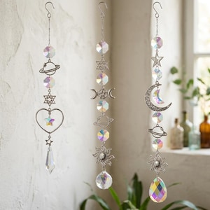 Peut inclure: Trois capteurs de soleil suspendus verticalement avec des breloques en métal argenté représentant des planètes, des étoiles, un cœur, un croissant de lune et un soleil. Chaque brin est orné de perles en verre irisé facetté et d'un prisme en cristal.