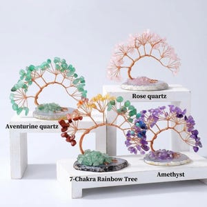 May include: Four decorative wire trees with gemstone leaves. One tree features green aventurine quartz, one has pink rose quartz, one has purple amethyst, and one is a 7-Chakra rainbow tree with multi-coloured stones. Each sits on a stone base.