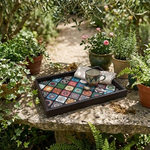 May include: A rectangular dark wood serving tray featuring a colourful mosaic pattern of square tiles with intricate mandala-style designs. The tray holds a ceramic mug with a blue and brown pattern, a folded white napkin, and a small silver spoon.
