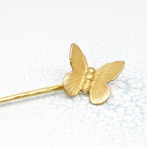 Op de afbeelding: Een gouden vlinder haarspeld met een textuur. De speld is ongeveer 10 cm lang en heeft een eenvoudig, elegant ontwerp.