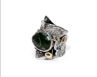 May include: A silver ring with a large, oval, dark green stone. The ring has a textured, organic design with gold accents. The stone is the focal point, set in a unique, handcrafted setting. The ring is a statement piece.