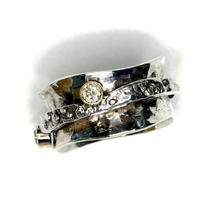 May include: A silver ring with a textured finish and a single diamond set in the band. The ring is designed to spin freely.
