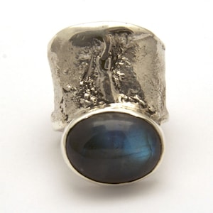 May include: A silver ring with a textured band and a large, round, dark blue gemstone.