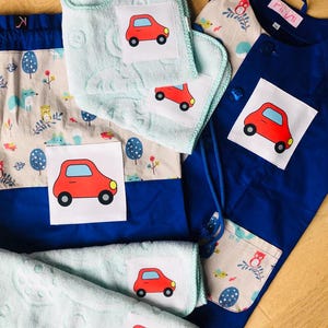 May include: A blue and beige fabric bag with a drawstring closure. The bag has a pocket with a print of owls and birds. The bag is accompanied by four light blue washcloths with red car appliques. The washcloths are made of soft, absorbent material. The bag and washcloths are perfect for a child's bathroom or playroom.