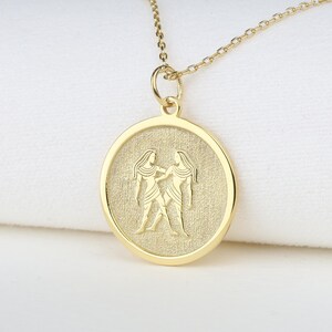 May include: Gold necklace with a round pendant featuring a zodiac symbol of Gemini. The pendant has a textured surface and the symbol is raised.