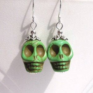 May include: A pair of green skull earrings with silver accents. The skulls are made of a green stone with a detailed carving of the skull features.