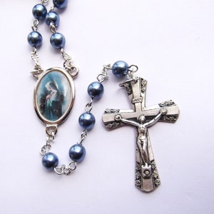 May include: A blue rosary with a silver crucifix and a silver oval pendant featuring a picture of the Virgin Mary. The pendant has a white background and the image is in color.