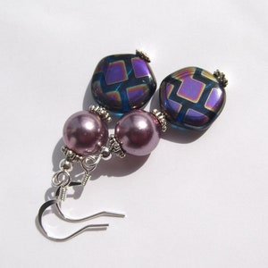 May include: A pair of earrings with iridescent purple and blue square patterned glass beads and mauve pearl beads.