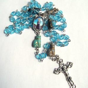 May include: A blue and silver rosary necklace with a religious charm and cat figurines. The beads are made of glass and the charms are made of metal.