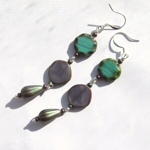May include: A pair of dangle earrings with purple and green glass beads. The earrings have silver hooks and are strung with small, dark purple beads.