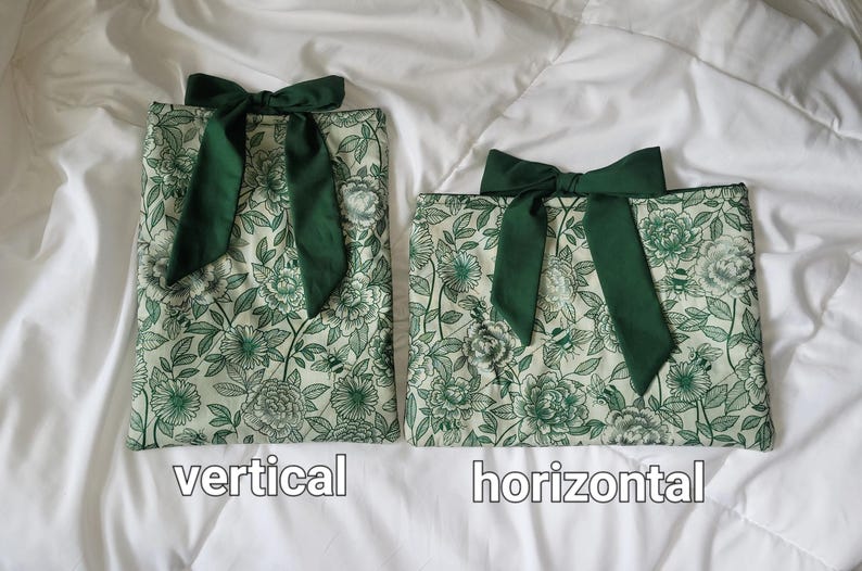 Peut inclure: Deux pochettes en tissu avec un motif floral et d'abeilles vert sur fond cr&egrave;me. Chaque pochette est orn&eacute;e d'un n&oelig;ud en tissu vert fonc&eacute; sur le dessus. La pochette de gauche est orient&eacute;e verticalement et celle de droite horizontalement.