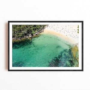 Könnte beinhalten: Eine Luftaufnahme eines Strandes mit klarem türkisfarbenem Wasser und einem Sandufer. Menschen schwimmen und sonnenbaden am Strand.