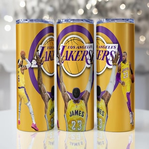 Puede incluir: Tres vasos de Los Angeles Lakers amarillos y morados. Cada vaso presenta el logotipo de los Lakers e imágenes de jugadores de baloncesto en acción. El texto "LOS ANGELES LAKERS" se muestra en cada vaso.