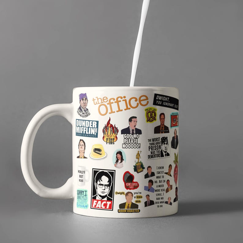 May include: White ceramic mug with a colourful design featuring characters and quotes from the TV show "The Office". The mug has a black handle and the words "The Office" are printed in black on the front.