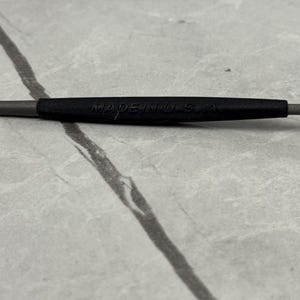 May include: Close-up of a gray and black tool with the text "MADE IN USA" printed on the black section. The tool is set against a light gray, marbled surface.