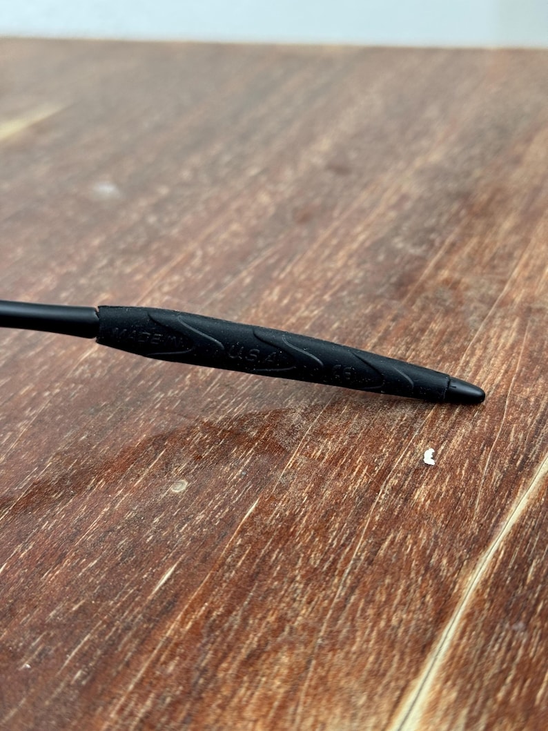 Op de afbeelding: Close-up van een zwart object met de tekst "MADE IN U.S.A." in reli&euml;f. Het object heeft een getextureerde grip en een puntig uiteinde. De achtergrond is een houten oppervlak.