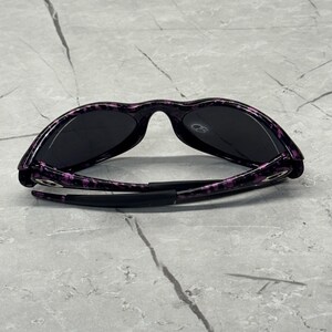 May include: Black sunglasses with a purple and black speckled pattern on the frames. The sunglasses have dark lenses and a sleek design. The arms are black and fold inwards.