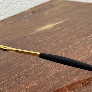 May include: Close-up of a pair of eyeglasses. The frame is gold-colored with a black arm. The arm has a black rubberized section for comfort. The glasses are resting on a wooden surface.