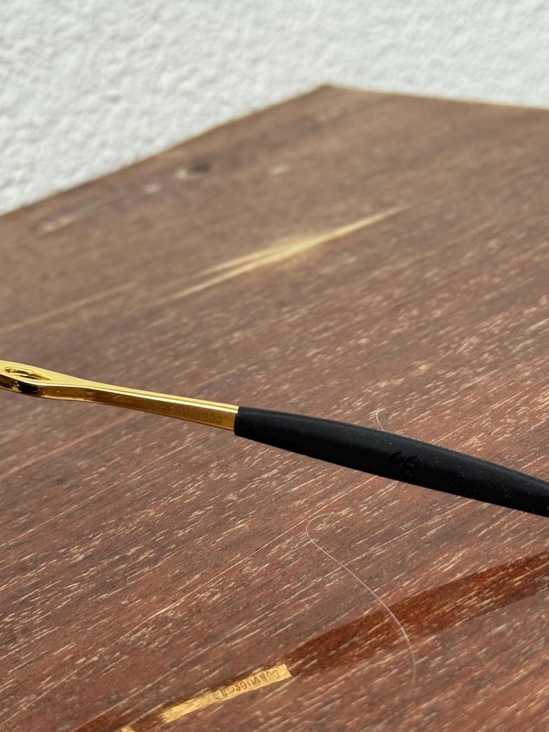 May include: Close-up of a pair of eyeglasses. The frame is gold-colored with a black arm. The arm has a black rubberized section for comfort. The glasses are resting on a wooden surface.