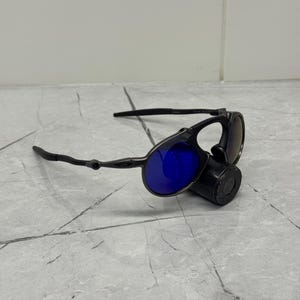 以下が含まれることがあります： 青いレンズの黒いサングラス。 サングラスは、暗いフレームと円筒形の黒いケースを備えた、洗練されたモダンなデザインです。 レンズは鮮やかな青色で、スタイリッシュな外観を提供します。