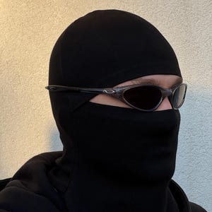 May include: Black balaclava with dark sunglasses. The balaclava covers the head and neck, with openings for the eyes and mouth. The sunglasses have a dark tint and a sleek, modern design.