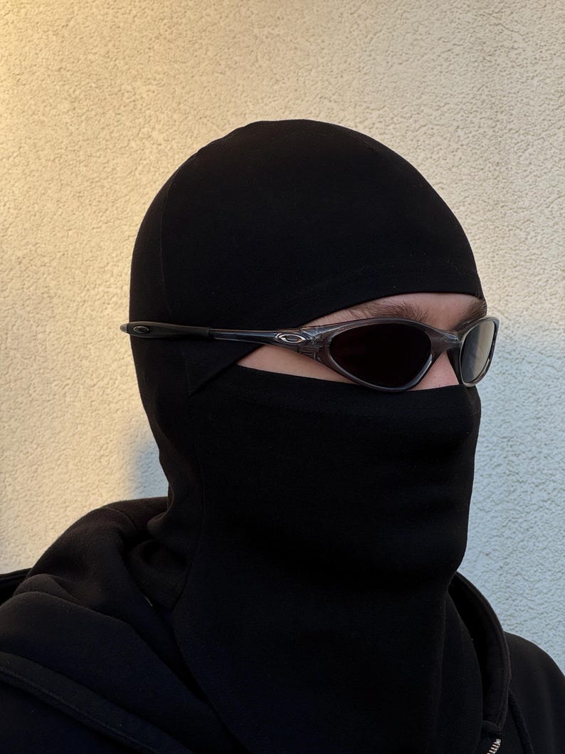 May include: Black balaclava with dark sunglasses. The balaclava covers the head and neck, with openings for the eyes and mouth. The sunglasses have a dark tint and a sleek, modern design.