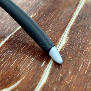 May include: A black stylus with a light blue tip. The stylus is angled towards the bottom right corner of the image. The background is a wooden surface with a brown color.