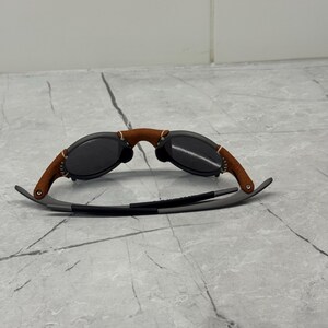 May include: Sunglasses with a brown leather bridge and temples, and dark lenses. The frames are a combination of gray metal and brown leather. The sunglasses are designed for eye protection and fashion.