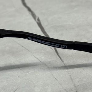 May include: Black eyeglasses frame with the word "MADMAN" printed in white on the temple. The frame is set against a light grey and white background.
