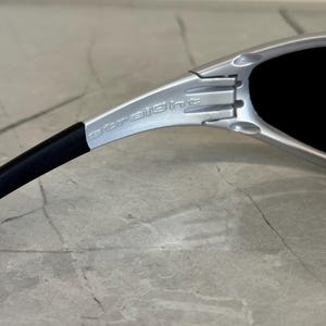 May include: Close-up of silver sunglasses with black lenses. The word "straight" is printed on the silver frame. The sunglasses have a sleek, modern design.