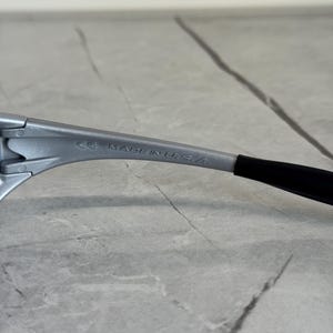 Puede incluir: Primer plano de una montura de gafas plateada con una patilla negra. El texto "MADE IN U.S.A." est&aacute; impreso en la montura.