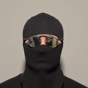 May include: A person wearing a black balaclava and sunglasses. The sunglasses have a silver frame and mirrored lenses. The balaclava covers the head and neck, leaving only the eyes visible.