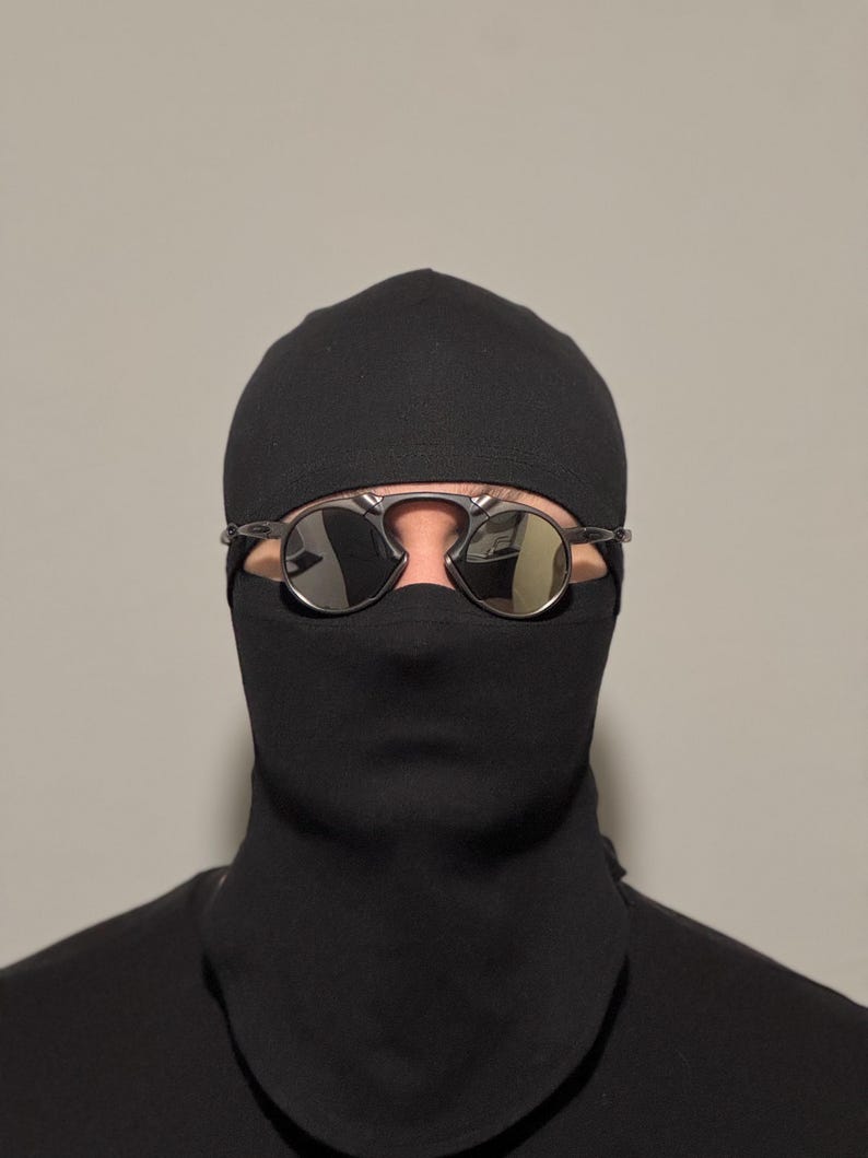May include: A person wearing a black balaclava and sunglasses. The sunglasses have a silver frame and mirrored lenses. The balaclava covers the head and neck, leaving only the eyes visible.