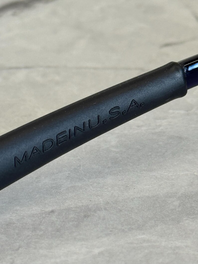 May include: Close-up of a black object with the embossed text "MADE IN U.S.A." The object has a smooth, matte finish and appears to be a handle or part of a larger tool. The background is a light gray, textured surface.