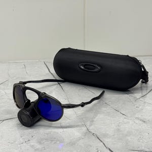 以下が含まれることがあります： 青いレンズと黒いケースが付いた黒いサングラス。 サングラスは、左側に丸いレンズと湾曲したフレームを備えたユニークなデザインです。 オーバル型のケースにはジッパーが付いています。