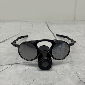 May include: Black sunglasses with circular lenses and a distinctive bridge. The sunglasses have a matte finish and a futuristic design. The lenses are reflective, and the frame is made of a durable material.
