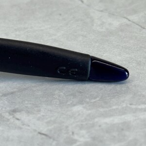 May include: Close-up of a black object with a dark blue tip. The object has the letters "CE" imprinted on it. The background is a light gray, textured surface.