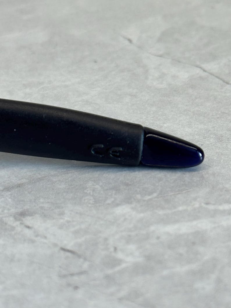 May include: Close-up of a black object with a dark blue tip. The object has the letters "CE" imprinted on it. The background is a light gray, textured surface.