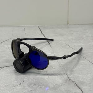 以下が含まれることがあります： 青いレンズの黒いサングラス。 サングラスは、黒いフレームと湾曲したテンプルを備えた、洗練されたモダンなデザインです。 レンズは鮮やかな青色で、スタイリッシュな外観を提供します。 サングラスは目の保護のために設計されています。