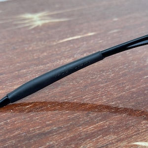May include: Close-up of a black object with the text "MADE IN U.S.A." printed on it. The object appears to be a part of a pair of glasses or sunglasses. The background is a wooden surface.