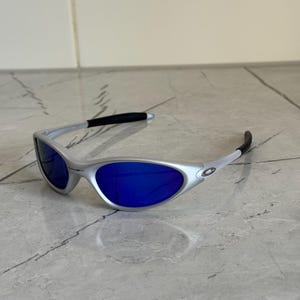 May include: Silver sunglasses with bright blue lenses. The modern design features a curved frame and black temple tips. These sunglasses offer a stylish look for outdoor activities.