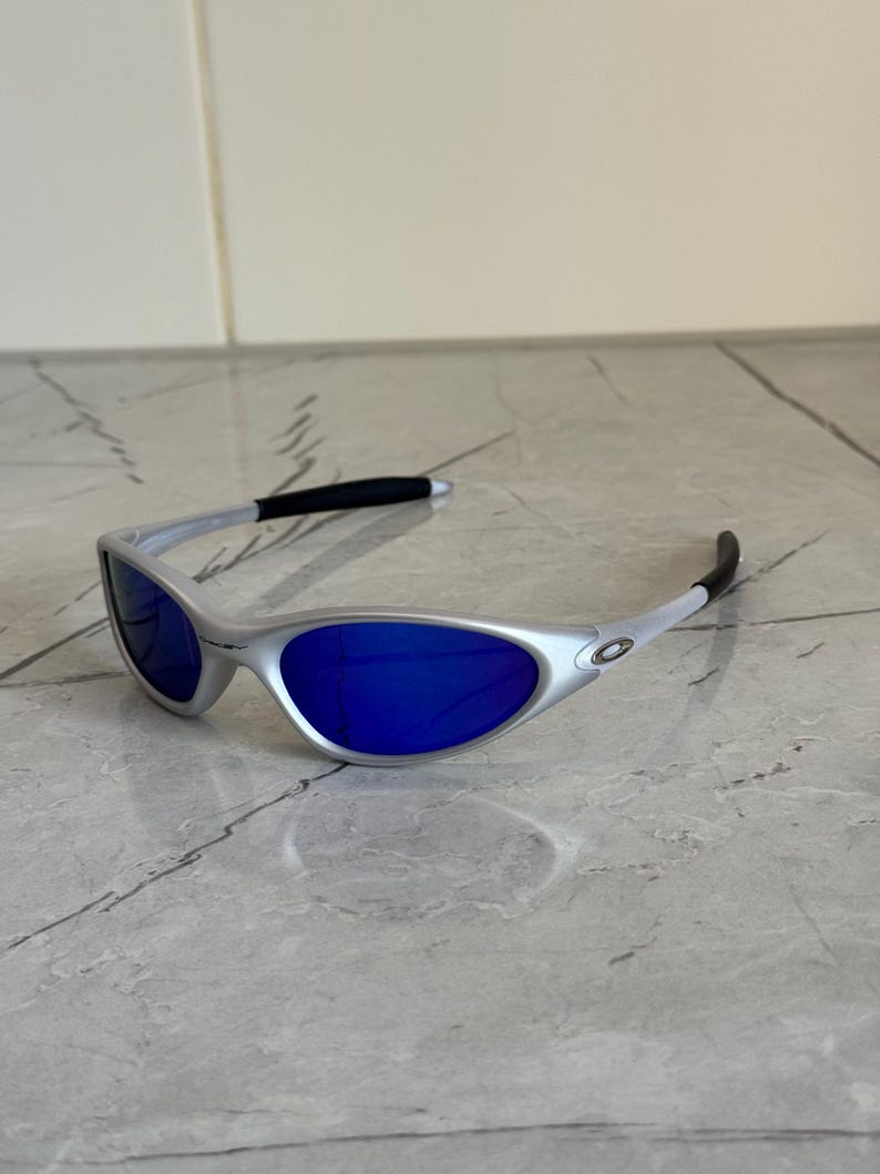 May include: Silver sunglasses with bright blue lenses. The modern design features a curved frame and black temple tips. These sunglasses offer a stylish look for outdoor activities.
