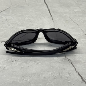 May include: Black sport sunglasses with a curved, wraparound design. The sunglasses have dark lenses and a matte black frame. The arms of the sunglasses are thin and feature silver accents near the hinges. The sunglasses are designed for sports and outdoor activities.